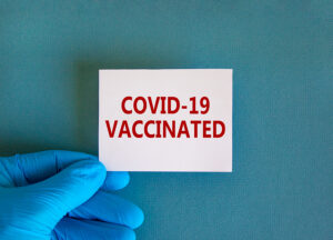covid 19 vaccinated symbol. hand in blue glove with white card.