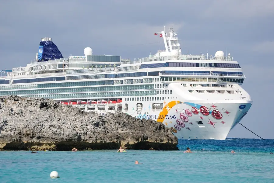 Norwegian Pearl cruise ship anchored near rocky shore in the Bahamas with swimmers in turquoise water, highlighting cruise tourism and safety.
