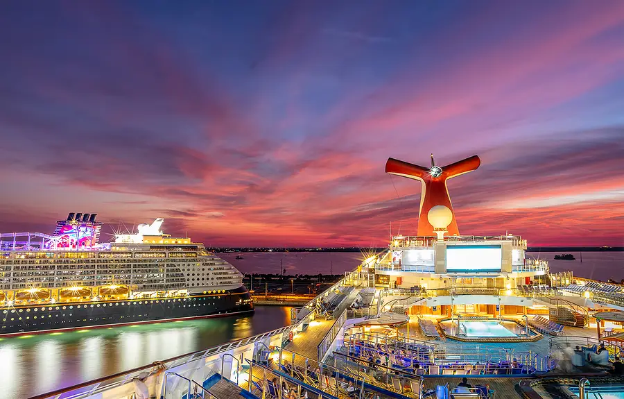 Carnival cruise ship docked at Port Canaveral during sunset, showcasing vibrant colors in the sky and illuminated deck features, symbolizing the resurgence of the cruise industry post-COVID-19.