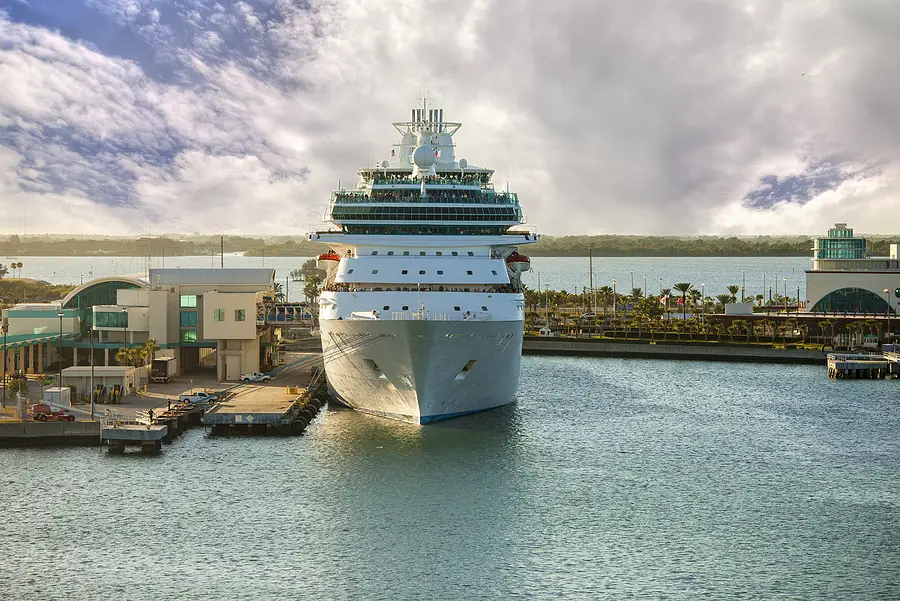 Cruise ship docked at Port Canaveral with terminal buildings and palm trees in the background, highlighting the resumption of cruise industry activities.