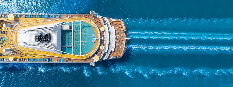 Aerial view of a large cruise ship with sports courts and deck chairs, sailing through blue waters, representing cruise travel experiences.