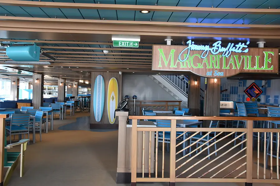 Interior of Margaritaville at Sea restaurant featuring colorful decor, exit sign, and seating arrangements, highlighting the cruise experience related to Margaritaville's offshore resort concept.