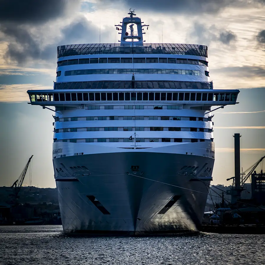 Cruise ship docking at port with cranes in the background, representing the cruise industry and maritime travel.