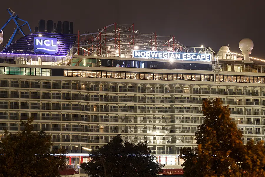 Norwegian Escape cruise ship with illuminated NCL logo, showcasing multiple decks and balconies, relevant to passenger rights and cruise incidents.