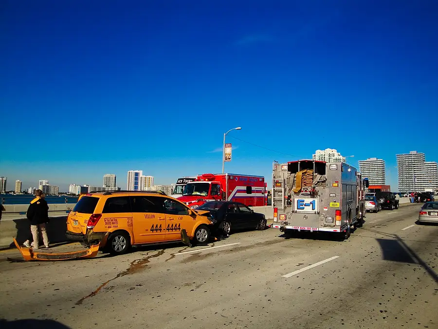 Taxi accident scene on a Florida road with emergency responders, damaged vehicles, and urban skyline in the background.