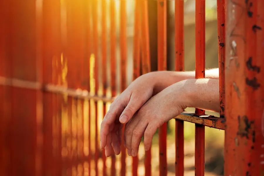 Hands resting on orange prison bars, symbolizing confinement and legal issues related to personal injury and crime.
