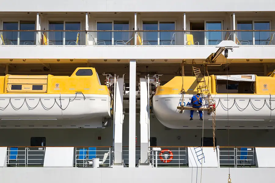 Worker inspecting lifeboats on a cruise ship, showcasing safety measures in maritime travel.