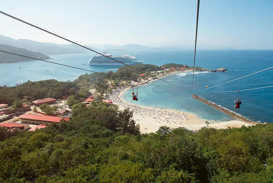 Zipline riders above a beach with a cruise ship in the background, showcasing a popular shore excursion destination.