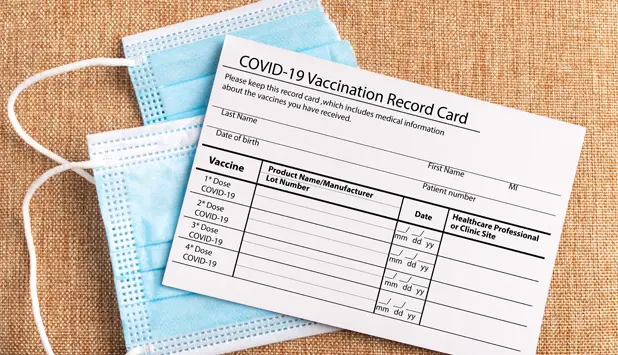 COVID-19 vaccination record card on a textured surface next to blue surgical masks, emphasizing vaccination requirements for cruise passengers.