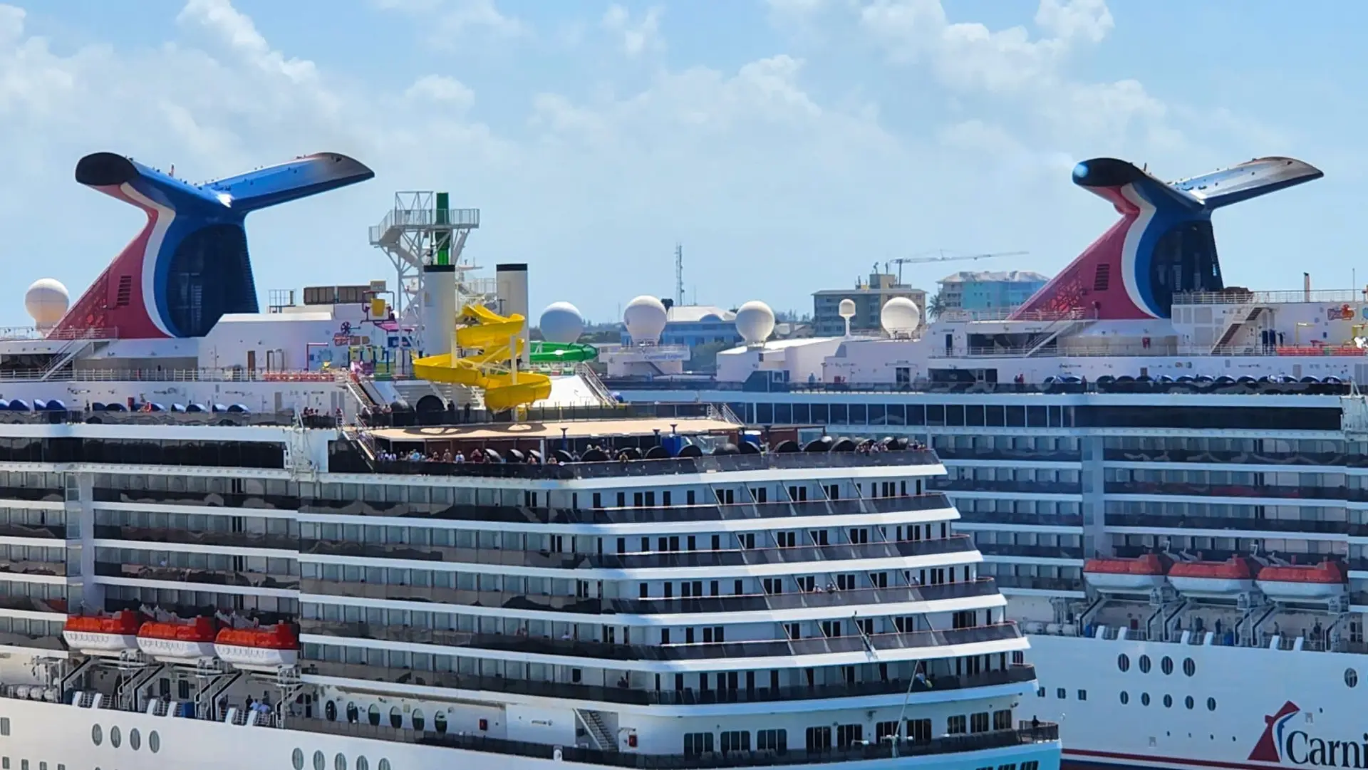 Carnival cruise ships docked, featuring colorful funnels, water slides, and passengers on deck, highlighting maritime travel and safety concerns.