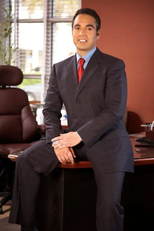 Abogado sonriente en traje profesional sentado en un escritorio, representando servicios legales de lesiones personales y accidentes en Florida.