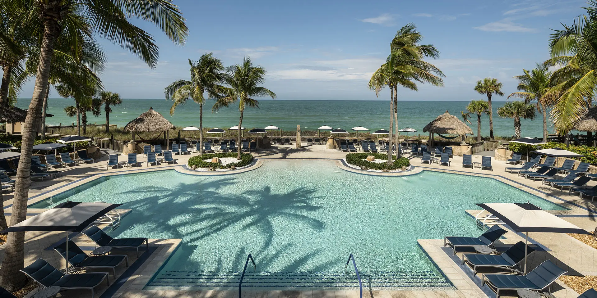 Resort-style swimming pool with lounge chairs and palm trees overlooking the Caribbean Sea, highlighting leisure and relaxation near cruise ship travel.