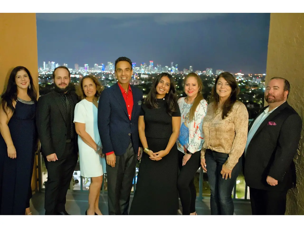 Group of individuals posing together in front of a city skyline at night, celebrating the holiday season, reflecting the community and safety themes of Aronfeld Trial Lawyers.