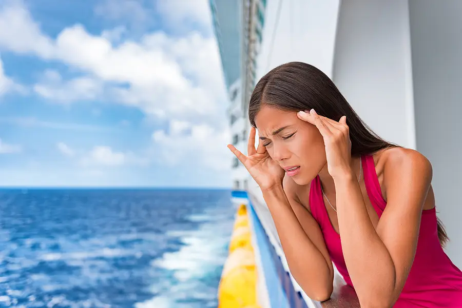 Woman experiencing seasickness on a cruise ship balcony, with ocean view and ship details in the background.