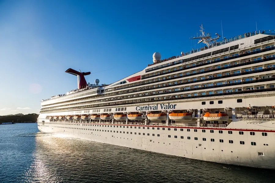 Carnival Valor cruise ship sailing in calm waters, showcasing multiple decks and lifeboats, relevant to discussions of cruise safety and personal injury incidents.