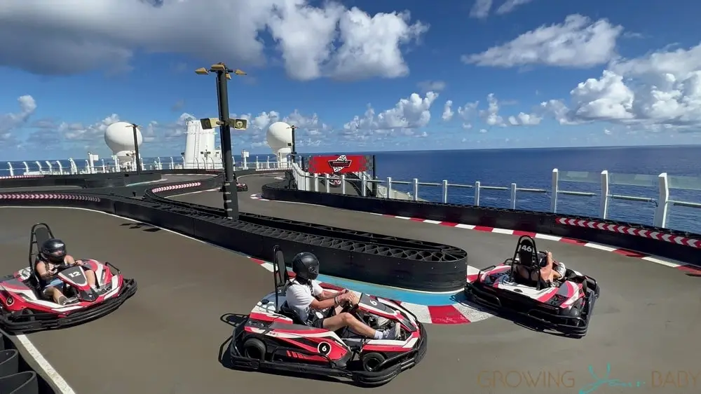 Go-kart racing on Norwegian Cruise Line's Encore Speedway, featuring three karts on a scenic track with ocean views and blue skies.