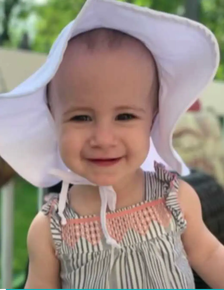 Toddler wearing a sun hat and striped dress, related to discussions on cruise ship safety and incidents involving children.