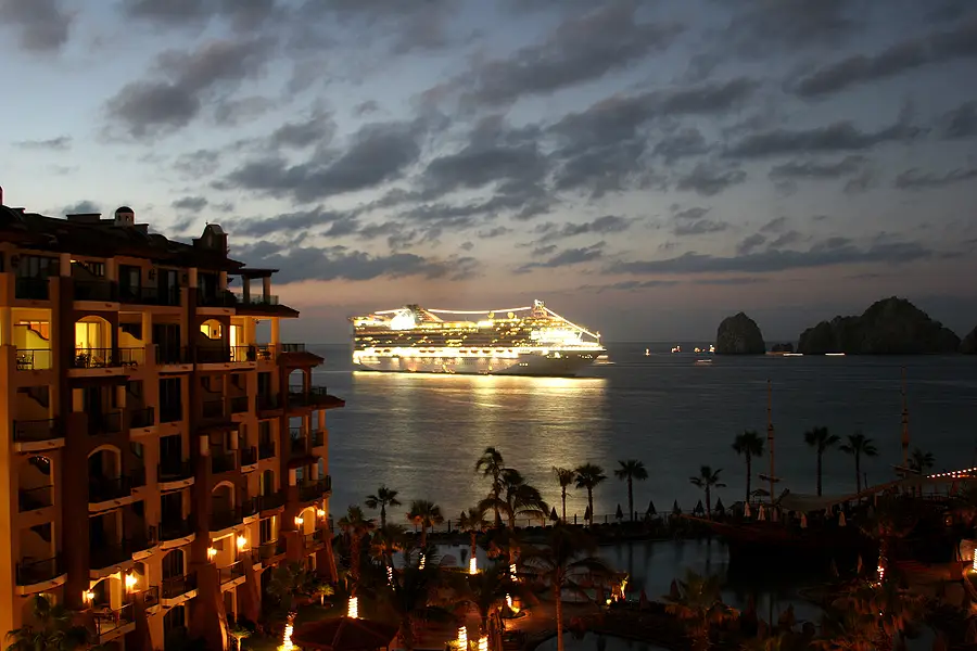 Cruise ship illuminated at night near coastal resort in Mexico, reflecting changes in itineraries due to cartel violence.